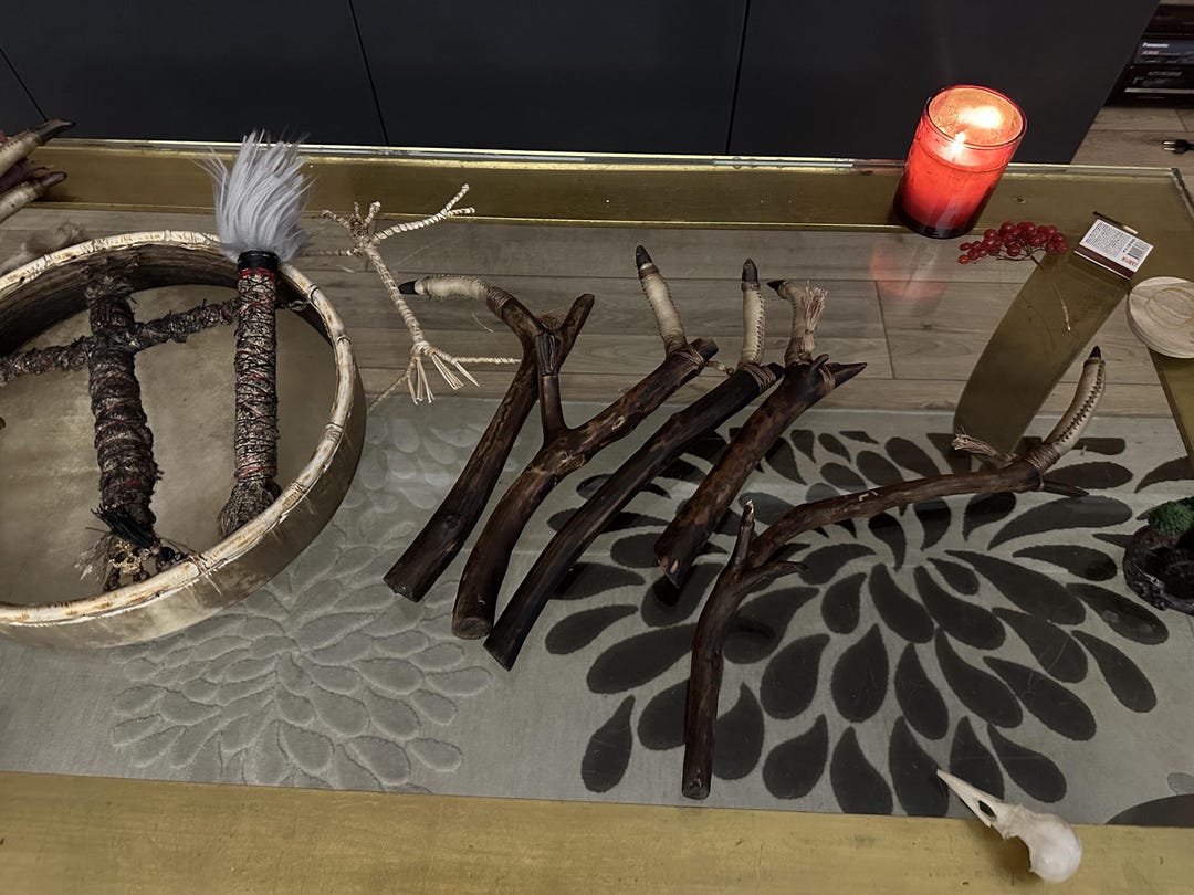Shaman's finger rattle beside a frame drum and a red candle on an altar